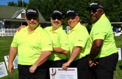 Group of golfers in green shirts in front of a hole sponsor sign