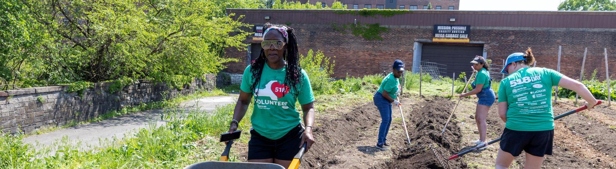 518 Day volunteers raking soil and pushing wheel barrel