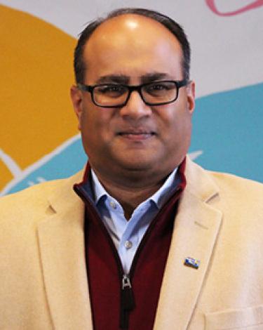 Alan in tan suit with red shirt smiling against colorful wall
