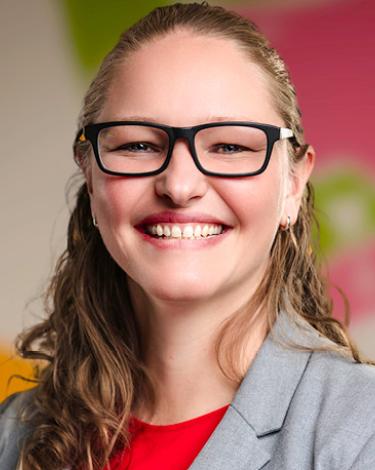 Kristie in glasses with gray suit red shirt against colorful wall