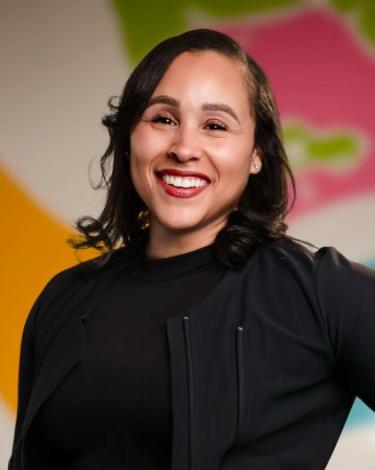 Ana smiling in black shirt against colorful wall
