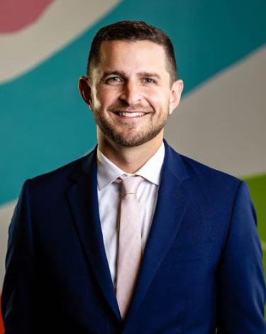 Kevin in blue suit and pink tie against colorful wall