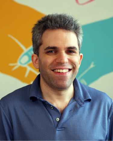 Andrew smiling in blue shirt against colorful wall