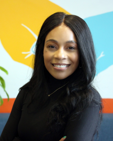 Angelique in black shirt smiling against colorful wall