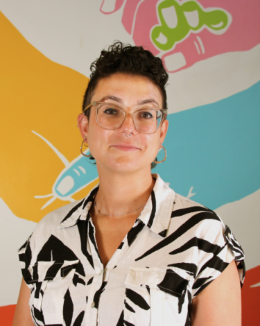 Antonia in black and white shirt smiling against colorful wall