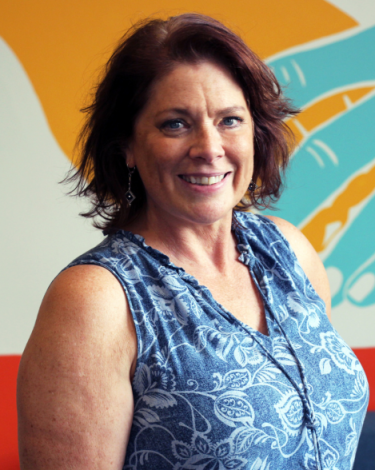 Gerri smiling in blue dress against colorful wall