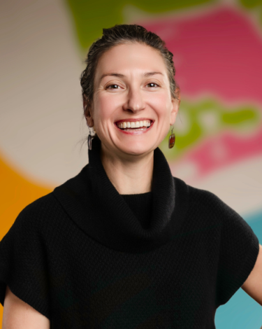 Heather in black turtleneck smiling against colorful wall