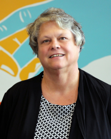 Kathi smiling in black top against colorful wall