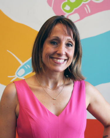 Nicki in pink dress smiling against colorful wall