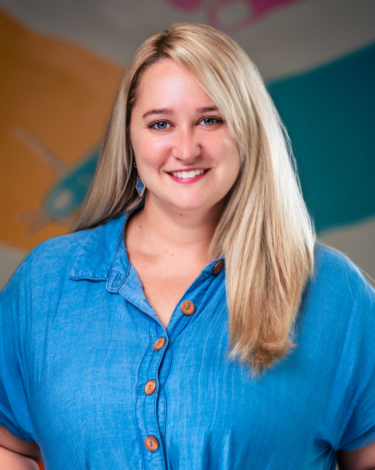 Sarah in blue dress smiling against colorful wall