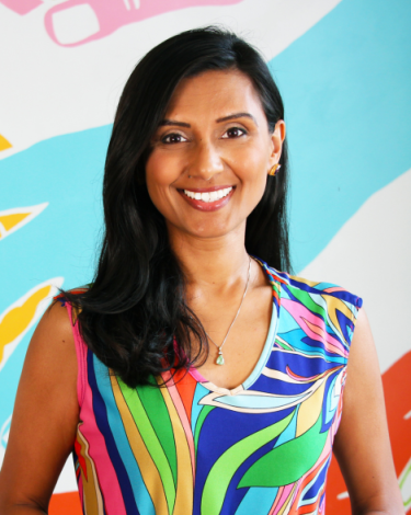 Trishna smiling in a colorful dress against colorful wall