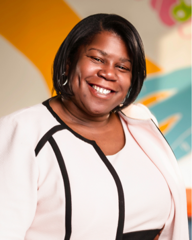 Yolanda smiling in white dress against colorful wall