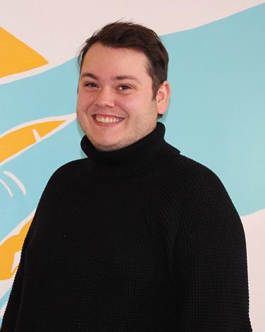 William in black turtleneck smiling against colorful wall