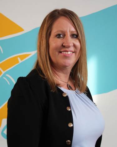 Erin Abele​ Smiling in lilac shirt and black blazer with large gold buttons